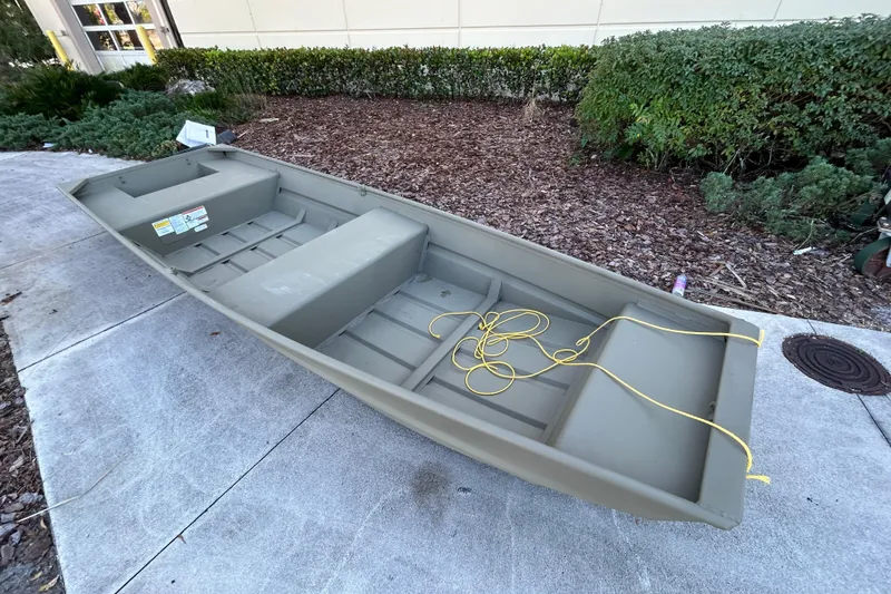Slide: The Image of 2026 Tracker Grizzly 14 Jon boat on concrete, with yellow rope, near shrubs. - 3