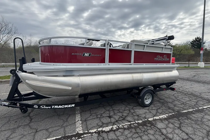 The Image of 2026 Sun Tracker Bass Buggy 16 XL Select pontoon boat on trailer, parked outdoors. - 0