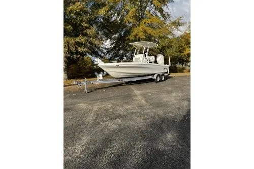 Slide: The Image of 2026 Mako 24 APEX boat on trailer, parked outdoors with trees in the background. - 1