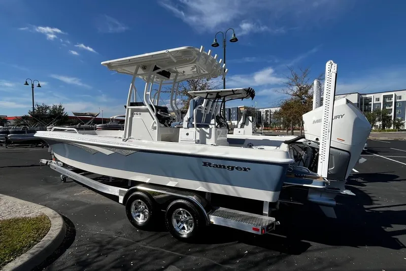 Slide: The Image of 2026 Ranger 2360 Bay boat on trailer, parked outdoors under clear blue sky. - 2