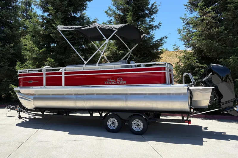 Slide: The Image of 2026 Sun Tracker Fishin' Barge 22 XP3 pontoon boat on trailer, parked outdoors. - 5