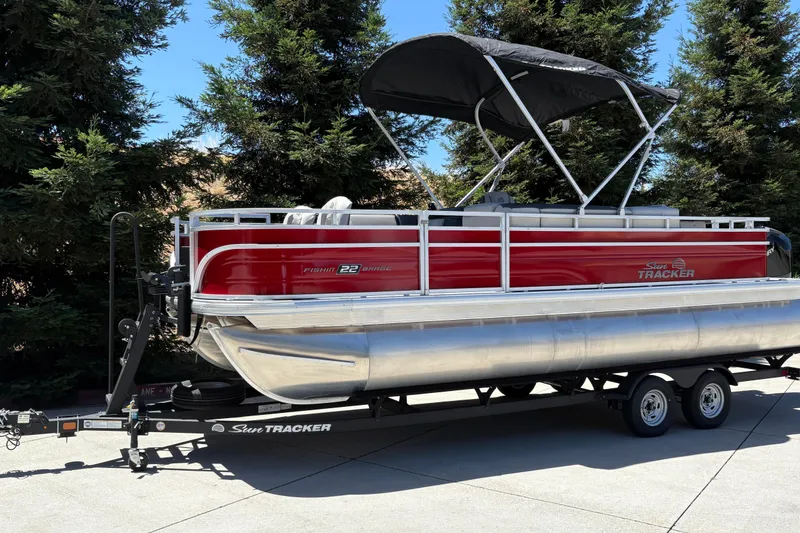 Slide: The Image of 2026 Sun Tracker Fishin' Barge 22 XP3 pontoon boat on trailer, parked outdoors. - 4