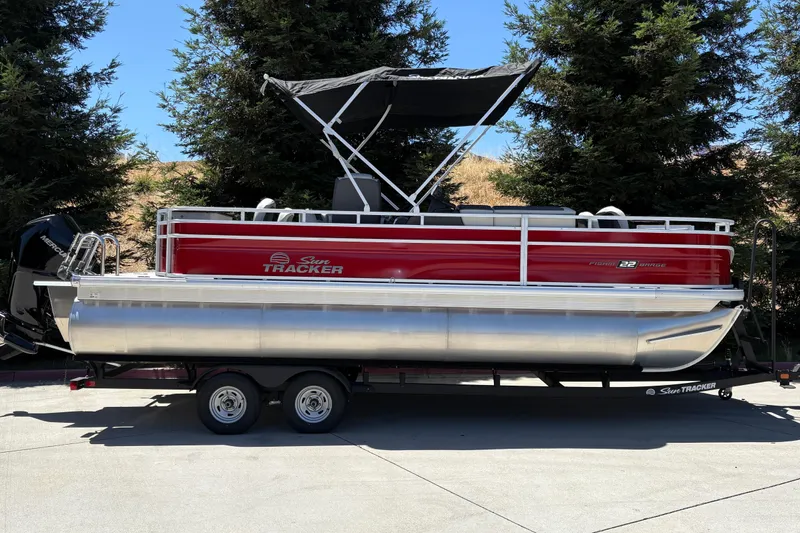The Image of 2026 Sun Tracker Fishin' Barge 22 XP3 pontoon boat on trailer, parked outdoors. - 0
