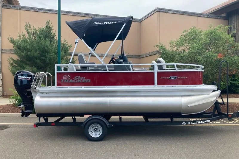 The Image of 2026 Sun Tracker Bass Buggy 16 XL Select pontoon boat on trailer, parked outdoors. - 0