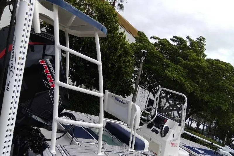 Slide: The Image of 2026 Mako 18 Pro Skiff Patriot Edition boat with Mercury Pro motor, docked near trees. - 10