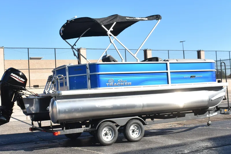 Slide: The Image of 2026 Sun Tracker Party Barge 20 DLX pontoon boat on trailer, featuring a Mercury outboard motor. - 2