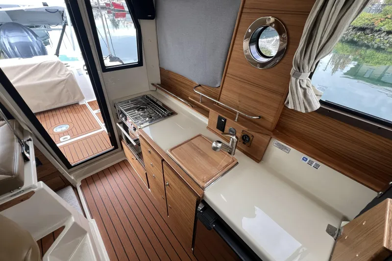Slide: The Image of 2025 Ranger Tugs R-27 Luxury Edition interior with kitchenette, wood finish, and window view. - 11