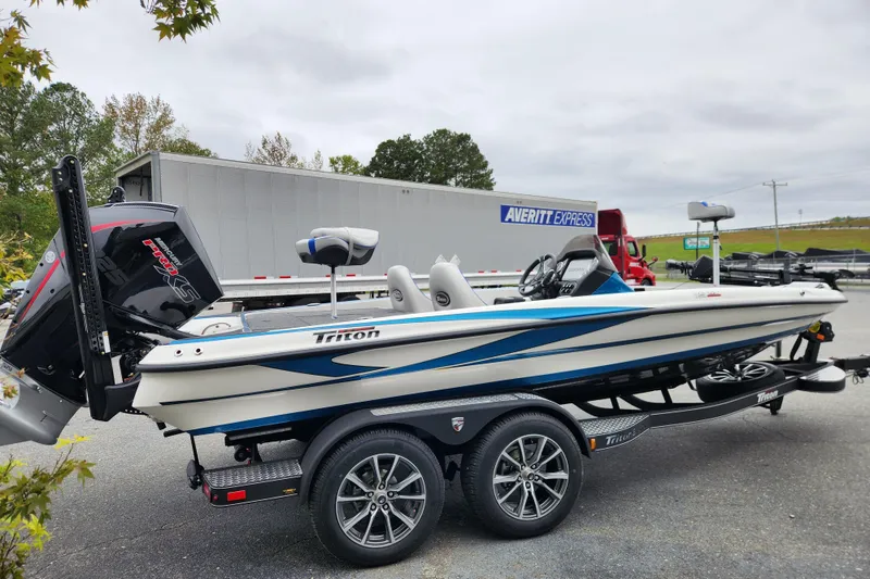Slide: The Image of 2026 Triton 19 TrX Patriot boat on trailer, parked near trucks. - 4