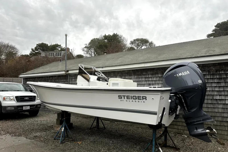 Slide: The Image of 2025 Steiger Craft 21 Classic boat with Yamaha engine on stands, parked beside a building. - 1