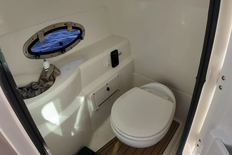 Slide: The Image of 2020 NauticStar 243 DC boat interior with compact marine toilet and porthole window. - 12