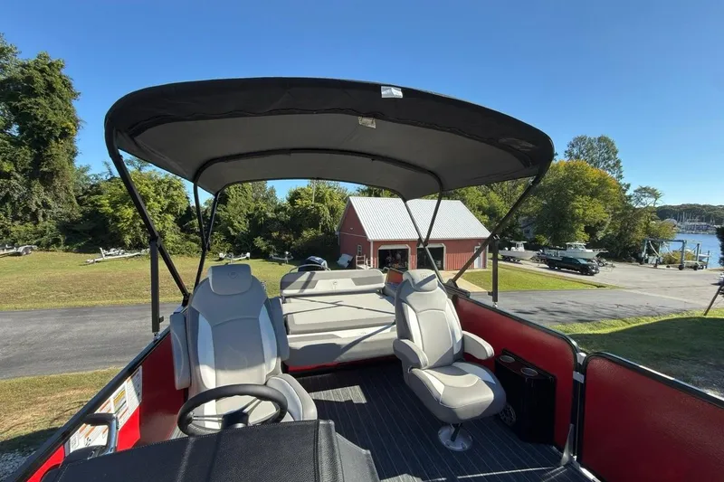 Slide: The Image of 2024 Premier 250 Solaris pontoon boat with canopy and seating, docked near a scenic marina. - 3