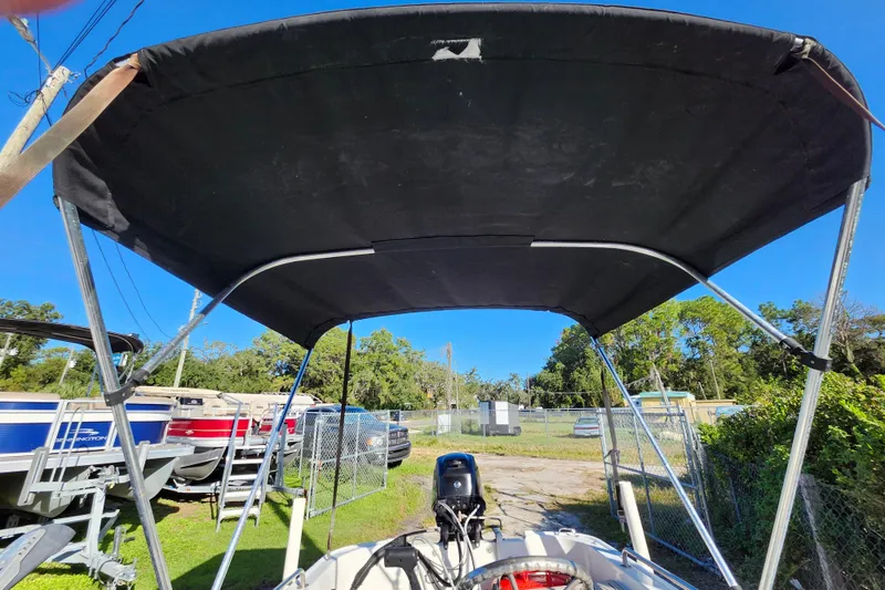 Slide: The Image of 2020 Boston Whaler 110 Sport with bimini top, parked outdoors under clear blue sky. - 10
