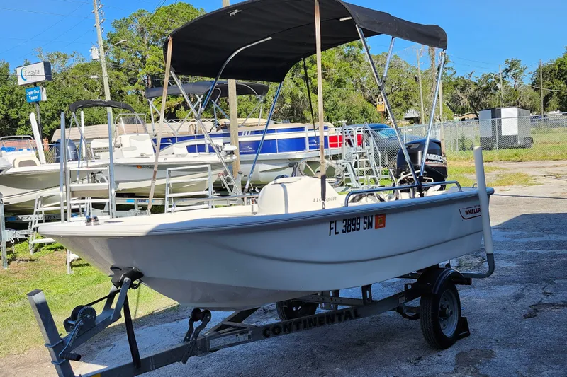 Slide: The Image of 2020 Boston Whaler 110 Sport boat on trailer with canopy, parked outdoors. - 3