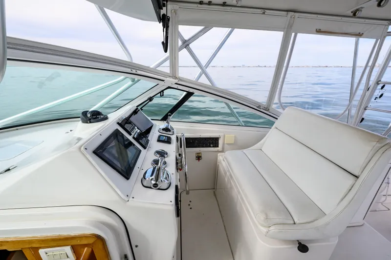 Slide: The Image of 1998 Bertram 36 Moppie boat cockpit with modern controls and white seating, overlooking calm waters. - 16