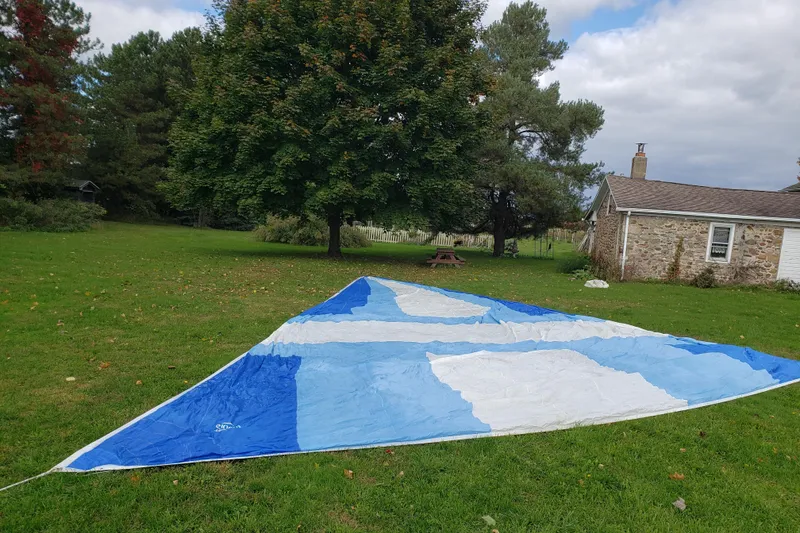 Slide: The Image of Blue and white sail on grass, near stone house and trees, Pearson 386, 1984. - 42