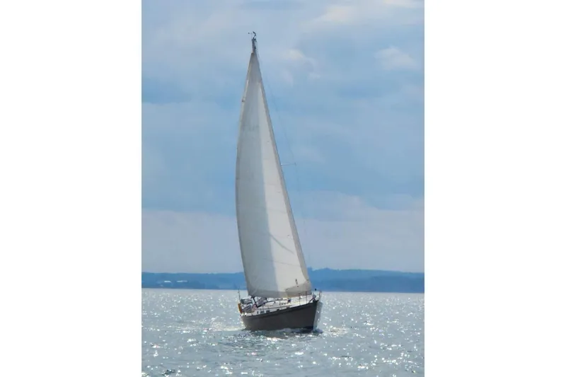 Slide: The Image of Sailboat Pearson 386 from 1984 gliding on shimmering water under a cloudy sky. - 2