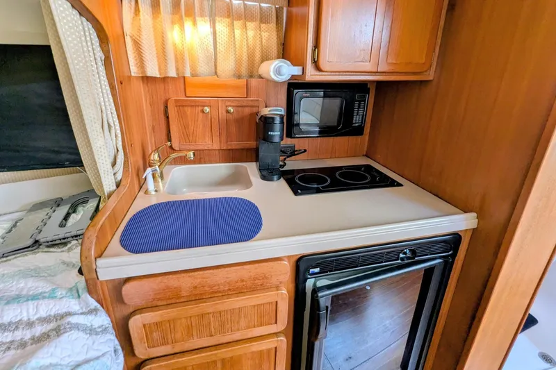 Slide: The Image of 2002 Stamas 340 Express boat kitchen with sink, stove, microwave, and wooden cabinetry. - 28