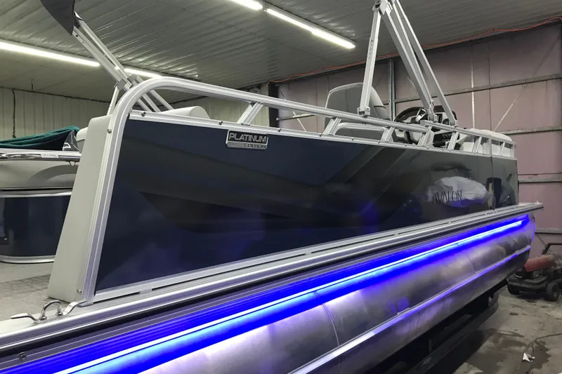 Slide: The Image of 2026 Avalon Venture 85 Versatile Rear Bench pontoon boat with blue LED lights in a garage. - 18