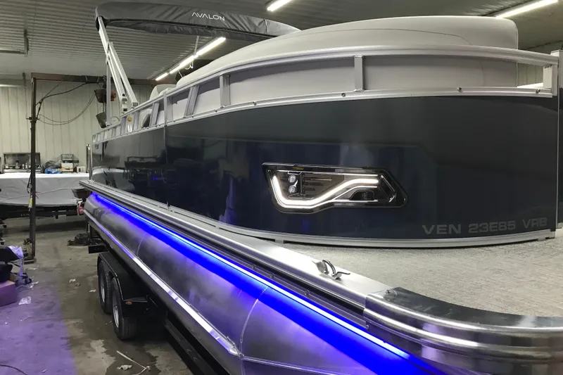 Slide: The Image of 2026 Avalon Venture 85 Versatile Rear Bench pontoon boat with blue LED lights in a garage. - 20