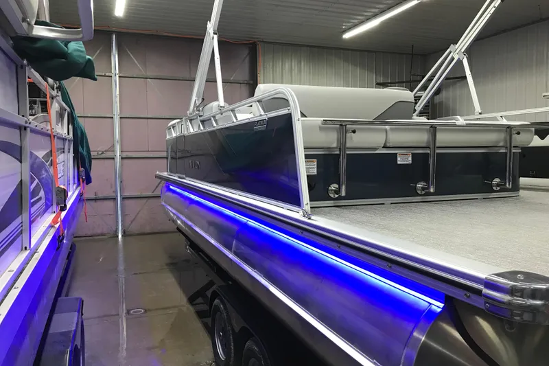 Slide: The Image of 2026 Avalon Venture 85 Versatile rear Bench pontoon boat with blue LED lights in a garage. - 24