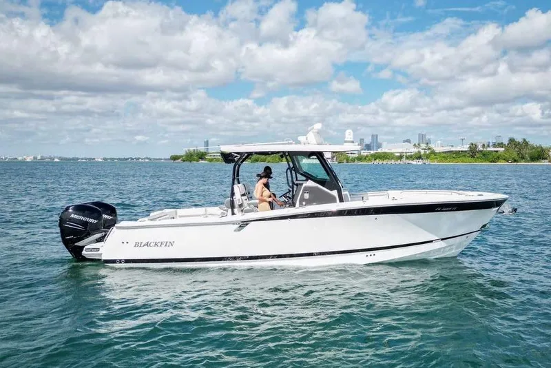 Slide: The Image of 2023 Blackfin 302 CC boat cruising on a sunny day with city skyline in background. - 8