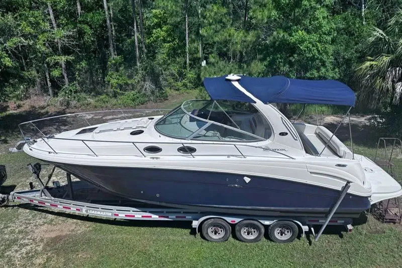 The Image of 2006 Sea Ray 300 Sundancer boat on trailer, surrounded by lush greenery. - 3