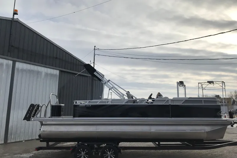 Slide: The Image of 2026 Avalon Venture Cruise Rear Bench pontoon boat on trailer, parked near industrial building. - 2