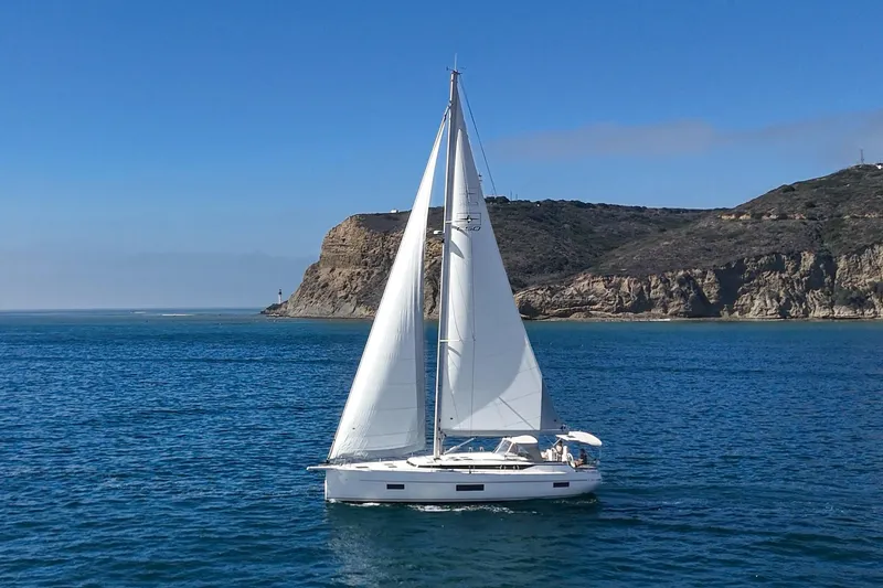 Slide: The Image of 2023 Bavaria C50 sailboat cruising near rocky coastline under clear blue sky. - 9