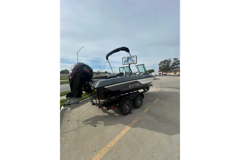Slide: The Image of 2026 Lund 185 Impact GL boat on trailer, parked outdoors with outboard motor. - 6