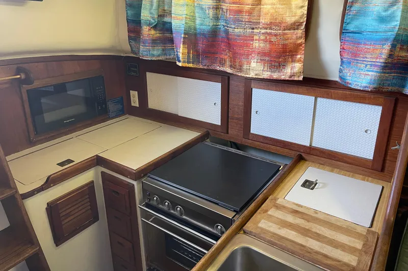 Slide: The Image of 1978 Downeast 38 boat kitchen with stove, microwave, and colorful curtains. - 22