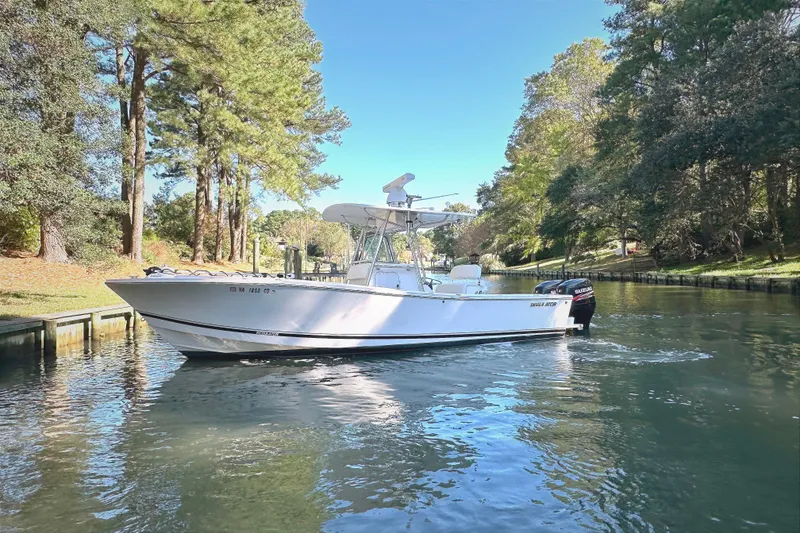 The Image of 2005 Regulator 26 Center Console boat cruising on a scenic, tree-lined waterway. - 1
