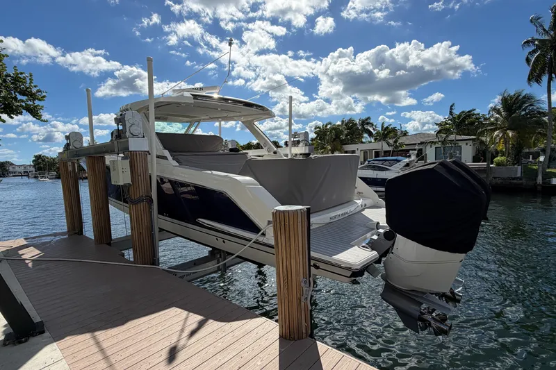 Slide: The Image of 2024 Tiara Yachts 43 LS on lift, docked by waterfront homes under a partly cloudy sky. - 41