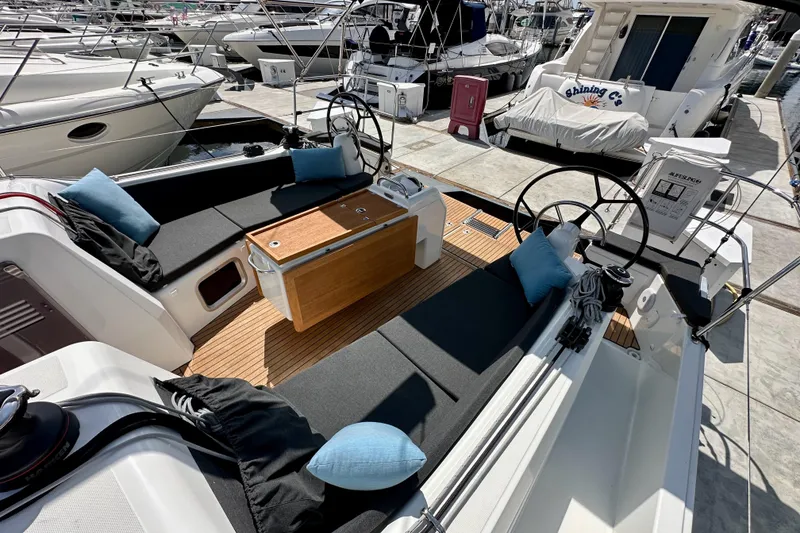 Slide: The Image of 2024 Jeanneau Sun Odyssey 410 yacht cockpit with seating, cushions, and steering wheels at a marina. - 62