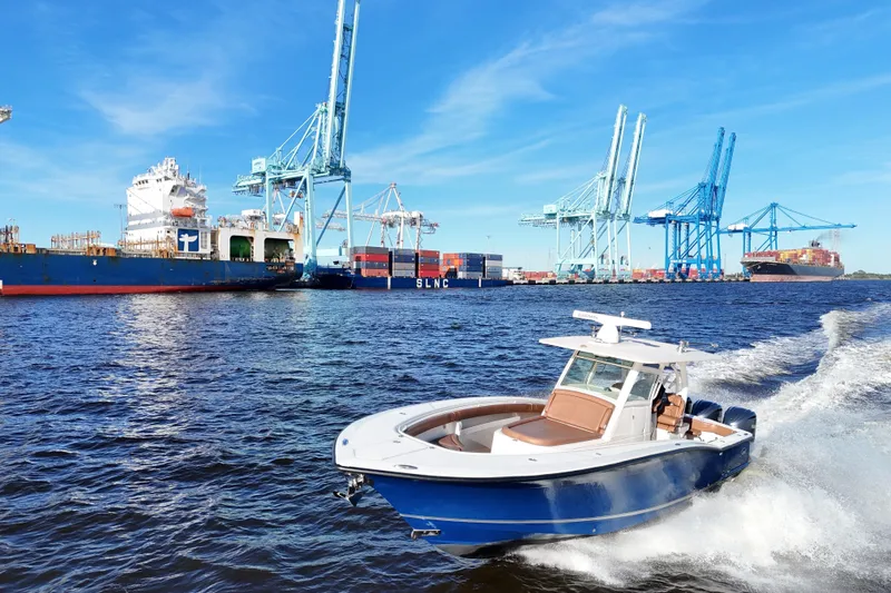 Slide: The Image of 2017 Scout 350 LXF boat cruising near a busy shipping port with cranes. - 23