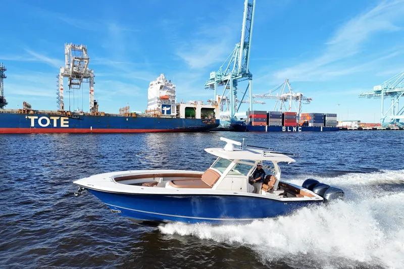 Slide: The Image of 2017 Scout 350 LXF boat cruising near cargo ships and cranes in a busy port. - 26