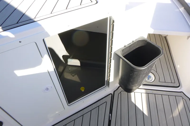 Slide: The Image of 2026 Yamaha Boats 222 FSH Sport E storage compartment with trash bin on deck. - 12