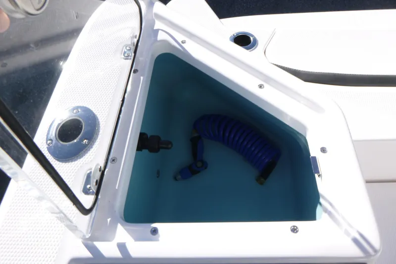 Slide: The Image of Open storage compartment on 2026 Yamaha Boats 222 FSH Sport E with coiled blue hose. - 19
