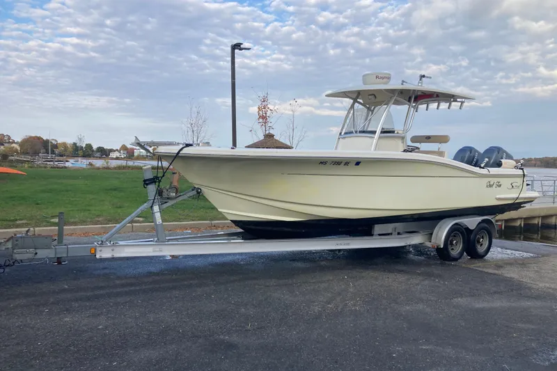 Slide: The Image of 2007 Scout 262 Sportfish boat on trailer, parked near a waterfront under cloudy sky. - 2