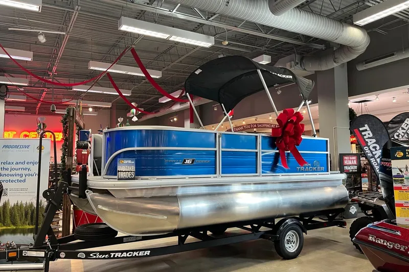The Image of 2026 Sun Tracker Party Barge 16 DLX pontoon boat displayed indoors with festive decorations. - 0
