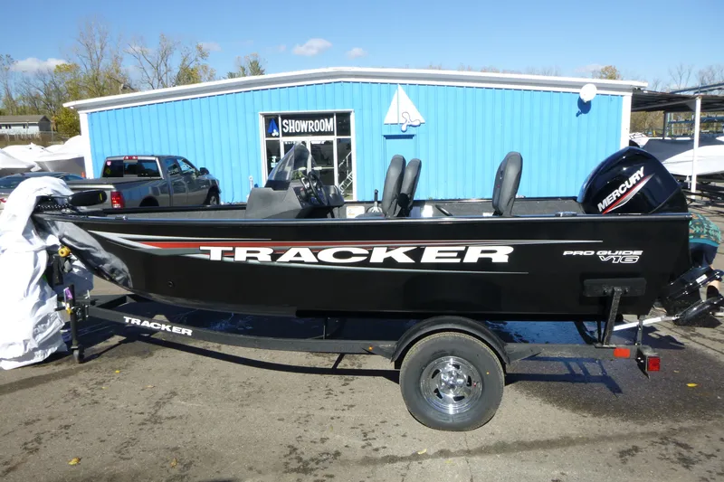The Image of 2026 Tracker Pro Guide V-16 SC boat displayed outside a blue showroom. - 1