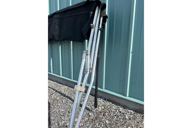 Slide: The Image of Folded bimini top frame for 2022 Four Winns HD2 OB boat, leaning against a metal wall. - 48