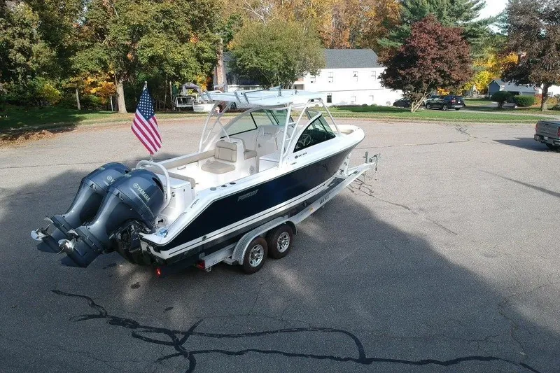 Slide: The Image of 2018 Pursuit DC 265 Dual Console boat on trailer with American flag, parked outdoors. - 6