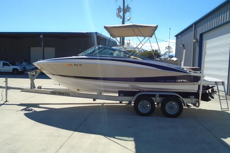 The Image of 2014 Regal 2300 Bowrider boat on trailer, parked outdoors near a warehouse. - 0