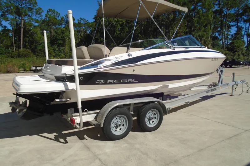 Slide: The Image of 2014 Regal 2300 Bowrider boat on trailer, parked outdoors with trees in background. - 2