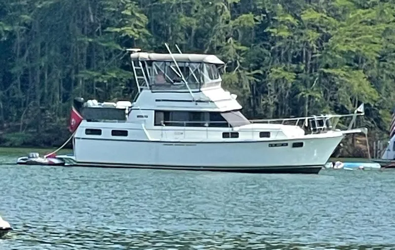 The Image of 1987 Carver 36 Aft Cabin Motor Yacht on a serene lake with forest backdrop. - 1