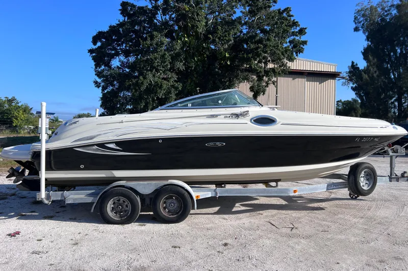 The Image of 2006 Sea Ray 240 Sundeck boat on trailer, parked outdoors under clear blue sky. - 0