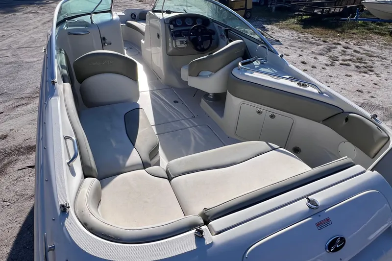 Slide: The Image of 2006 Sea Ray 240 Sundeck interior with spacious seating and helm, parked on sandy ground. - 12
