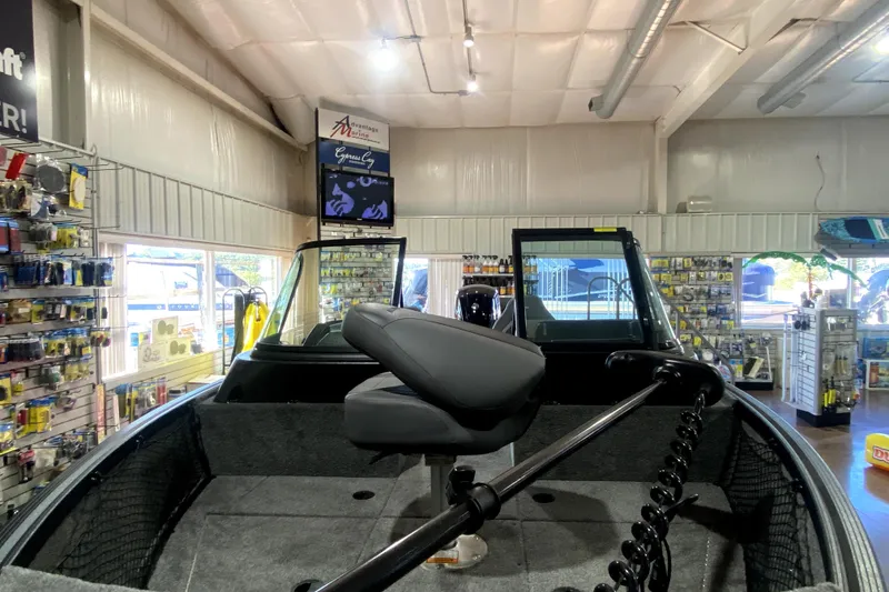 Slide: The Image of 2026 Alumacraft Voyageur 175 Sport boat displayed in a showroom with fishing gear. - 12