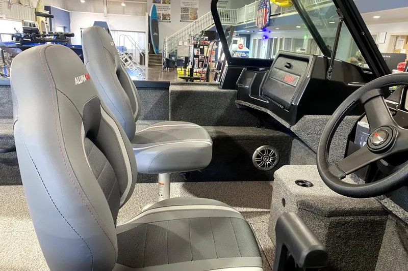 Slide: The Image of 2026 Alumacraft Voyageur 175 Sport interior with gray seats and steering wheel in showroom. - 6