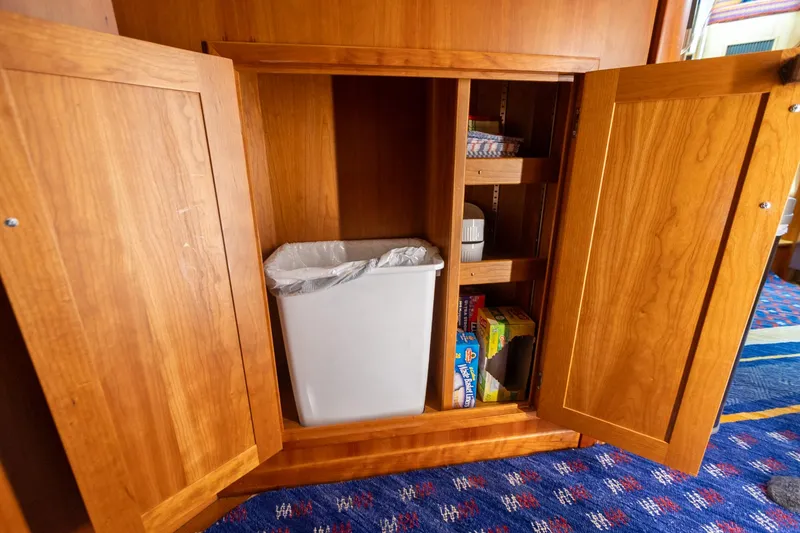 Slide: The Image of Wooden cabinet with open doors, revealing a trash bin and shelves, on a Sabre 52 Express yacht. - 32